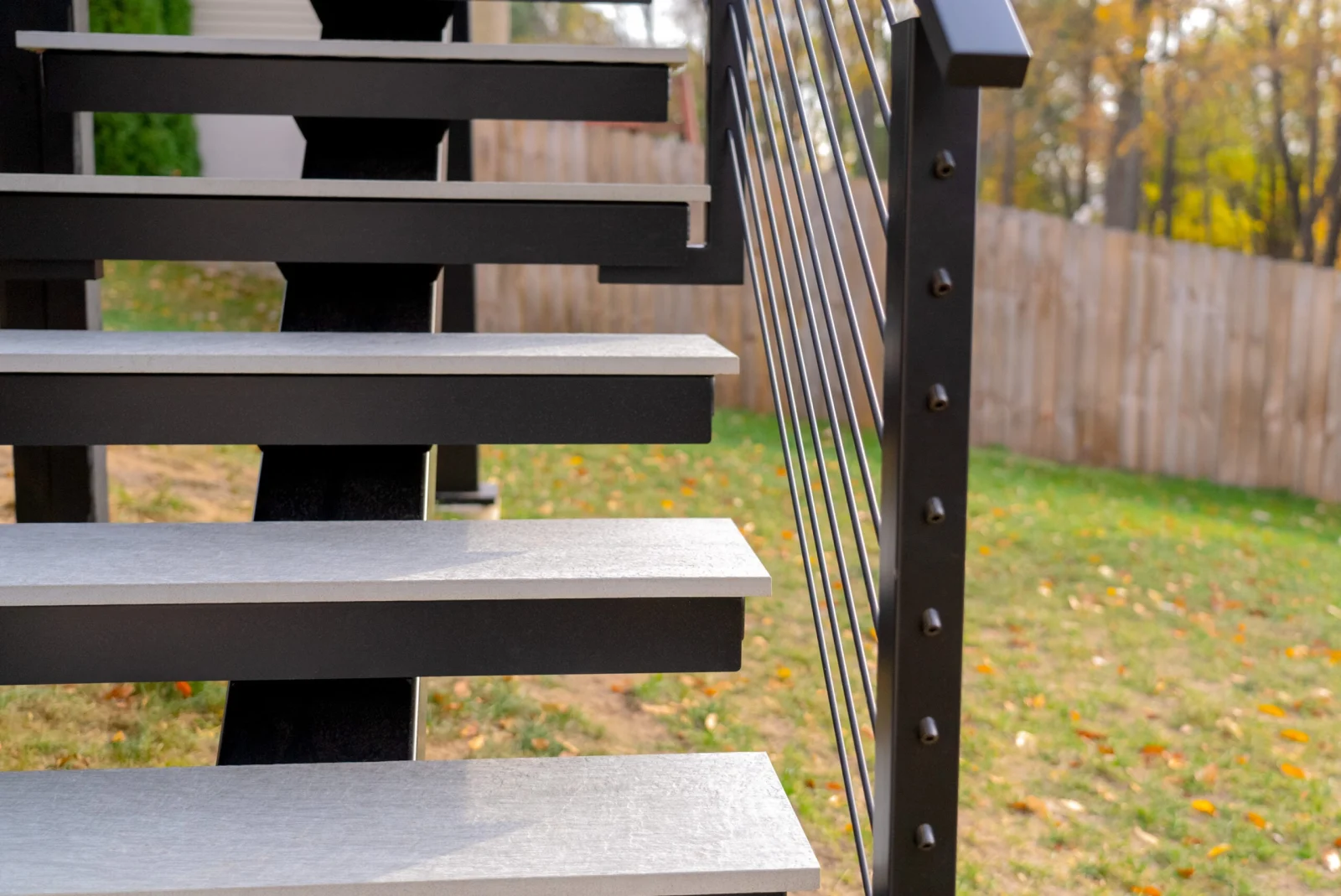 Stone treads on a black stringer beside a rod railing post above the lawn