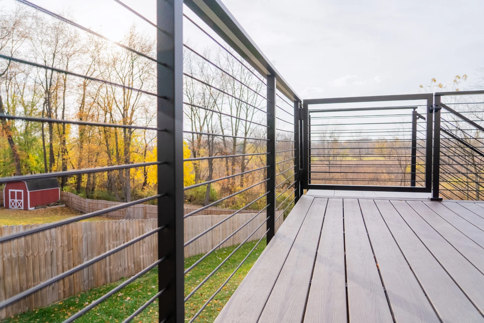 Gray deck boards beside a long run of black rod railing facing open fields