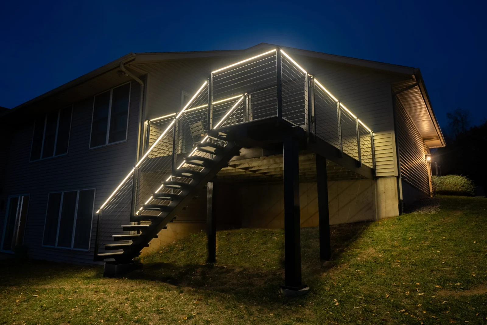 Night view of the deck and stair outlined by lit railing against the house