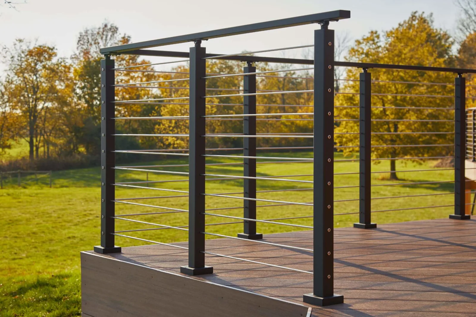 Black posts and stainless rods edging a deck with autumn trees in the distance