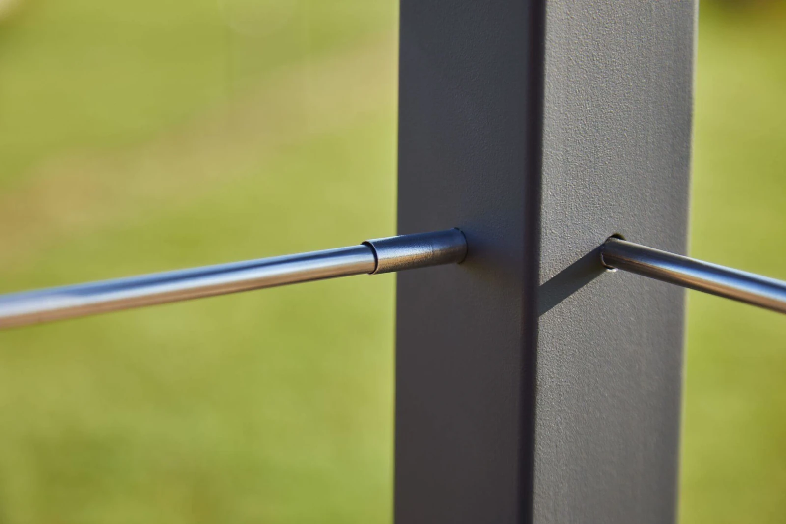Macro view of stainless rods entering a black post against a grassy yard