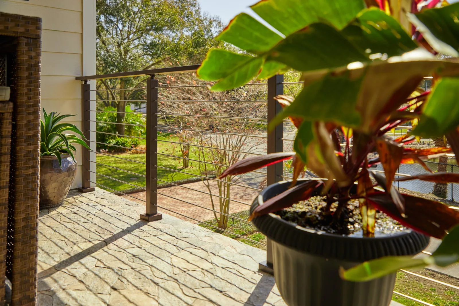 Copper-toned rod railing edging a stone patio framed by potted tropical plants