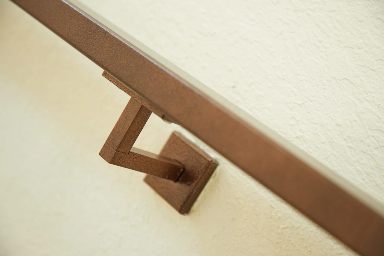 Close view of a bronze wall bracket supporting a flat-profile handrail