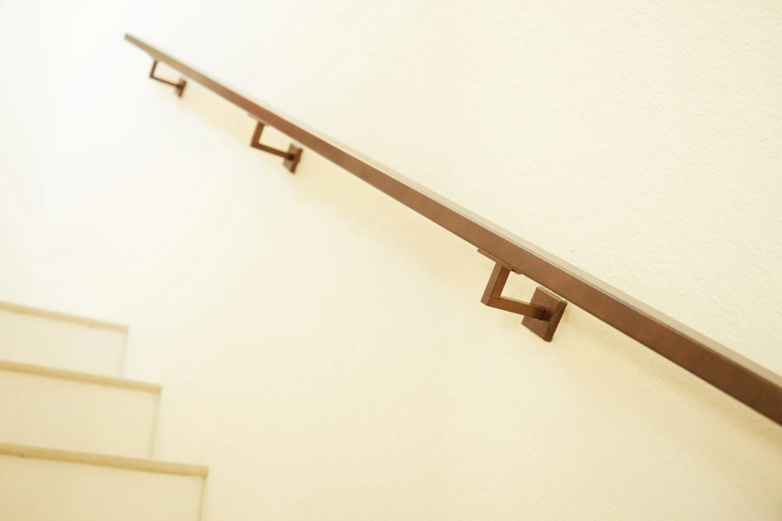 Wall-mounted handrail angling up a plaster wall above pale stair treads