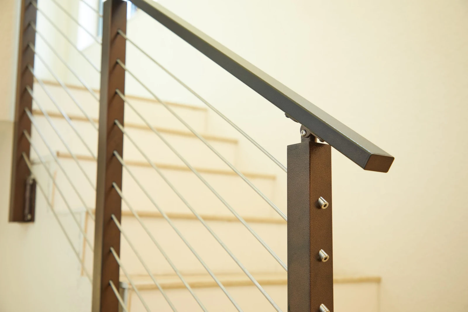 Bronze post capped by a dark top rail with stainless rods along the stair