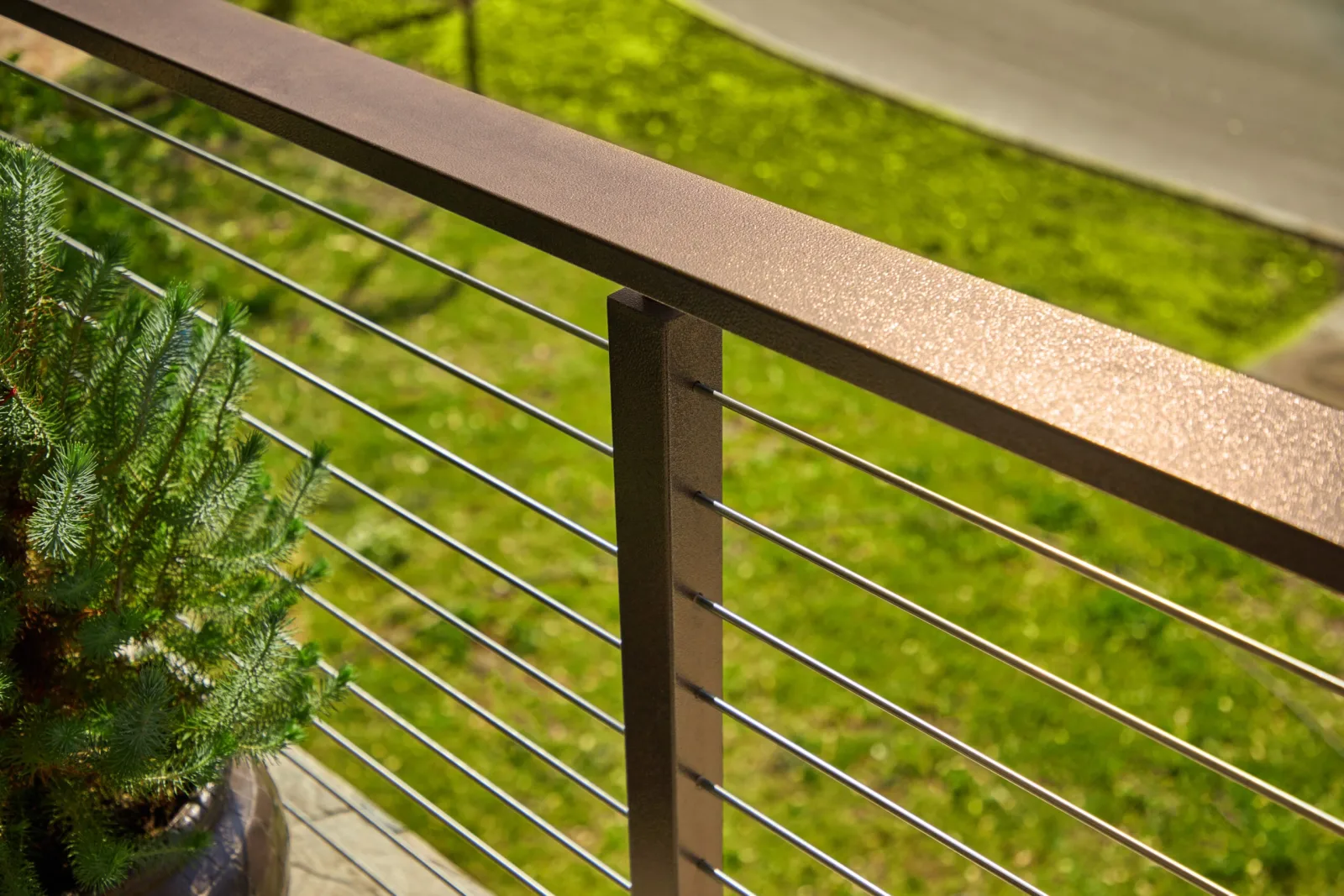 Textured top rail and stainless rods angling above a sunlit green lawn