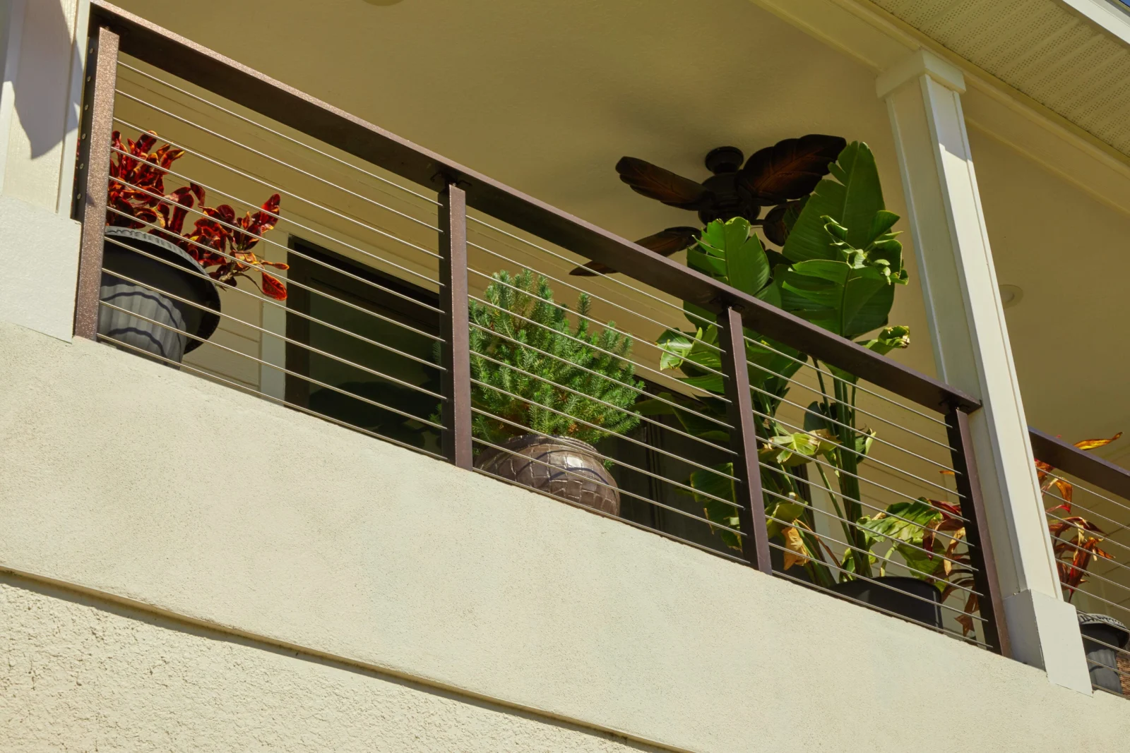 Second-floor balcony railing with rods and potted greenery seen from below