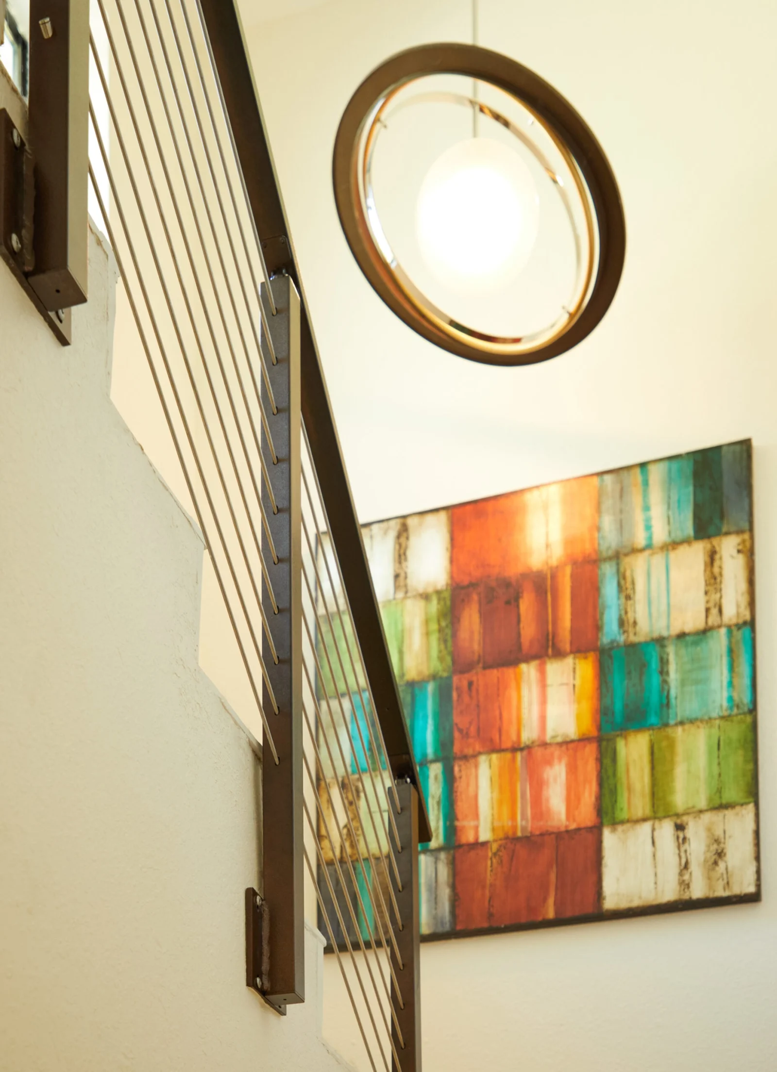 Stairwell railing beside a round pendant light and a color-blocked canvas
