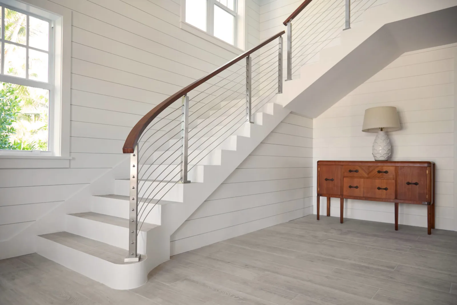 Curved white stair with horizontal rod infill under a shaped wood handrail in shiplap hall
