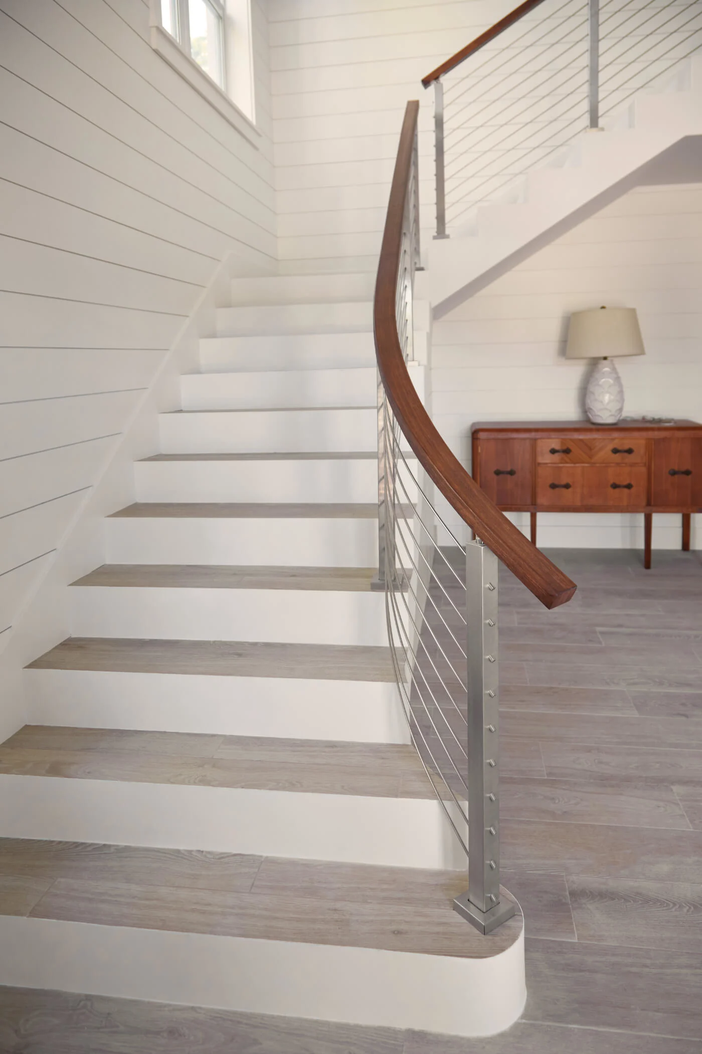 Curved stair with white risers, light treads and stainless posts with rod infill