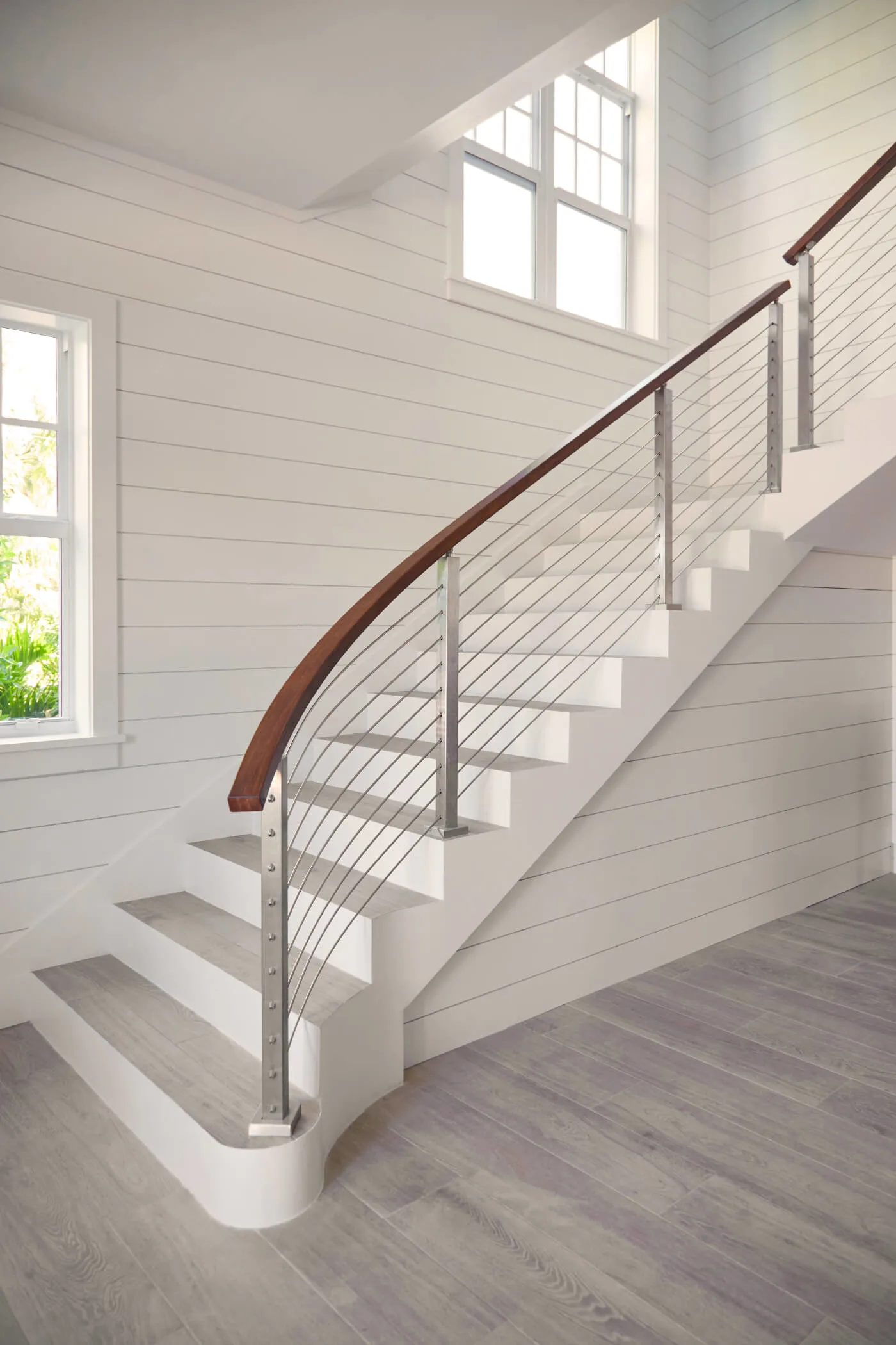 Curved stair against shiplap walls with a sweeping wood handrail over rods