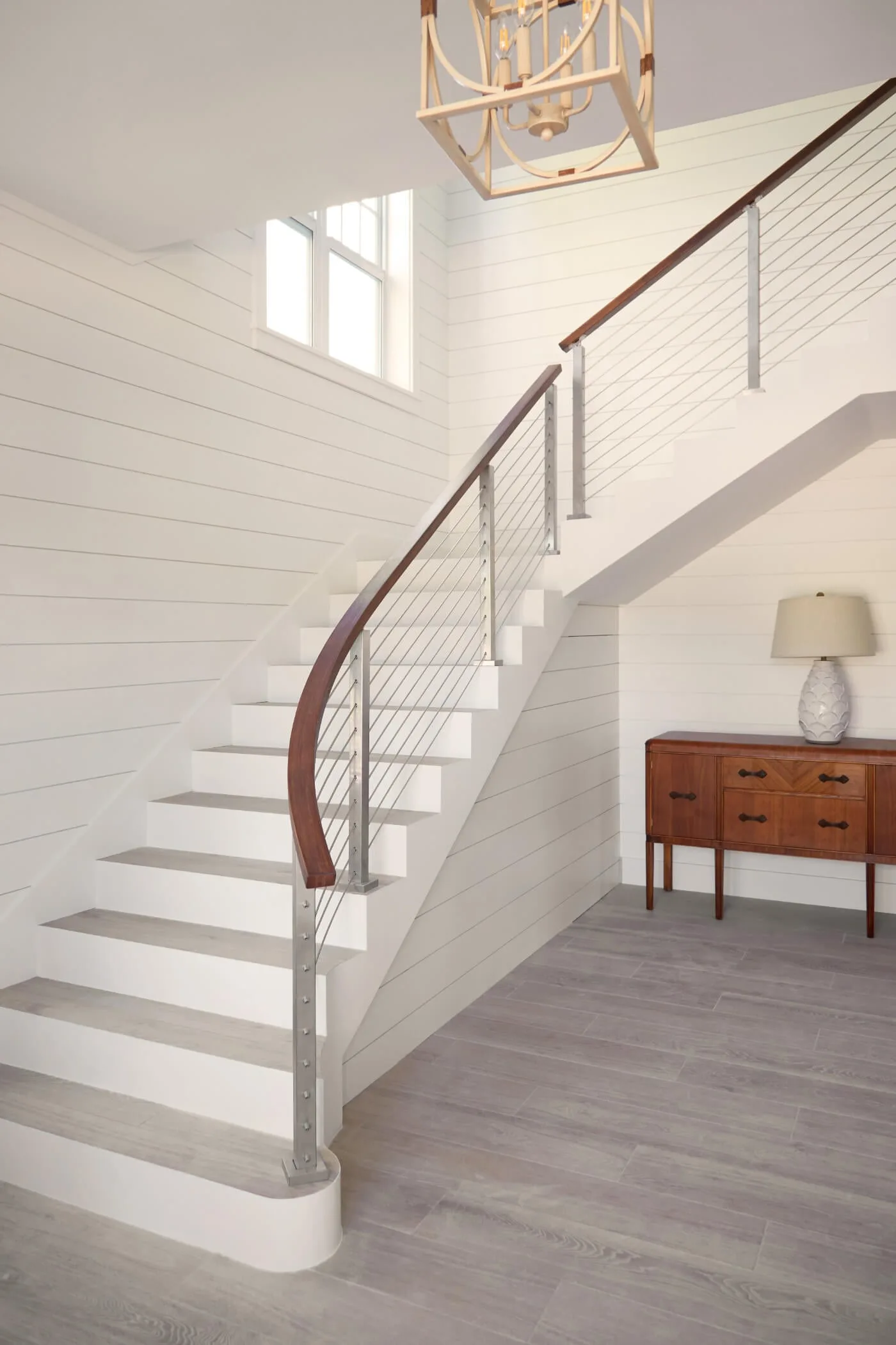 Stair hall with lantern pendant, dresser and curved rod railing climbing right