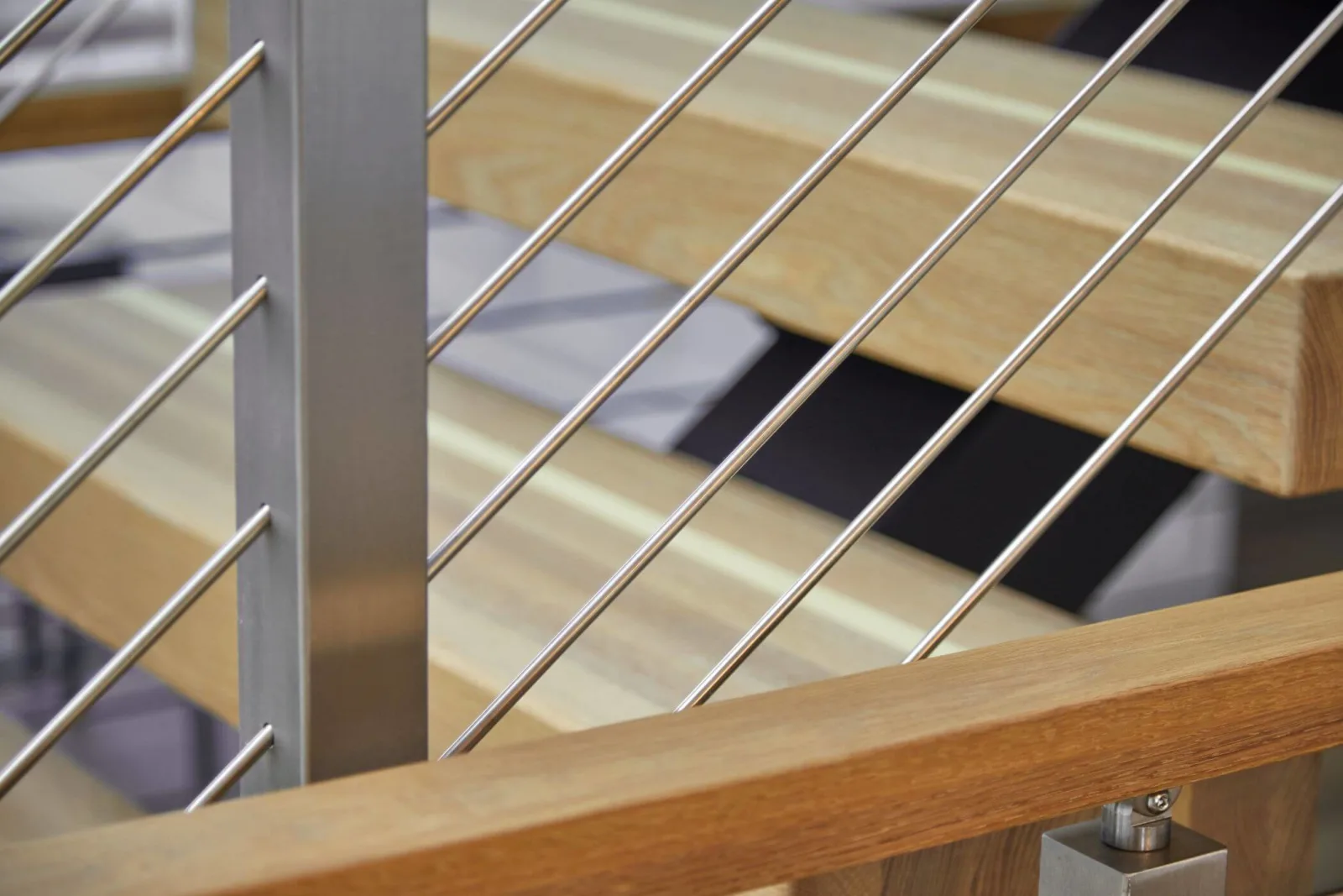 Stainless rods and a brushed post crossing behind a wood handrail and floating treads