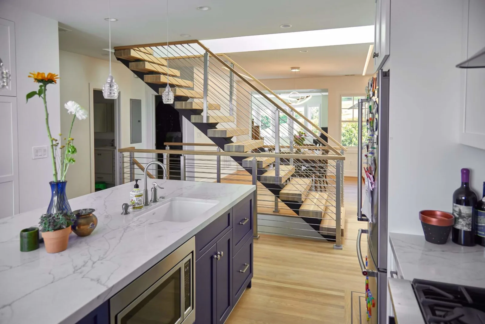 Marble kitchen island in front of a floating stair with metal posts and horizontal rods