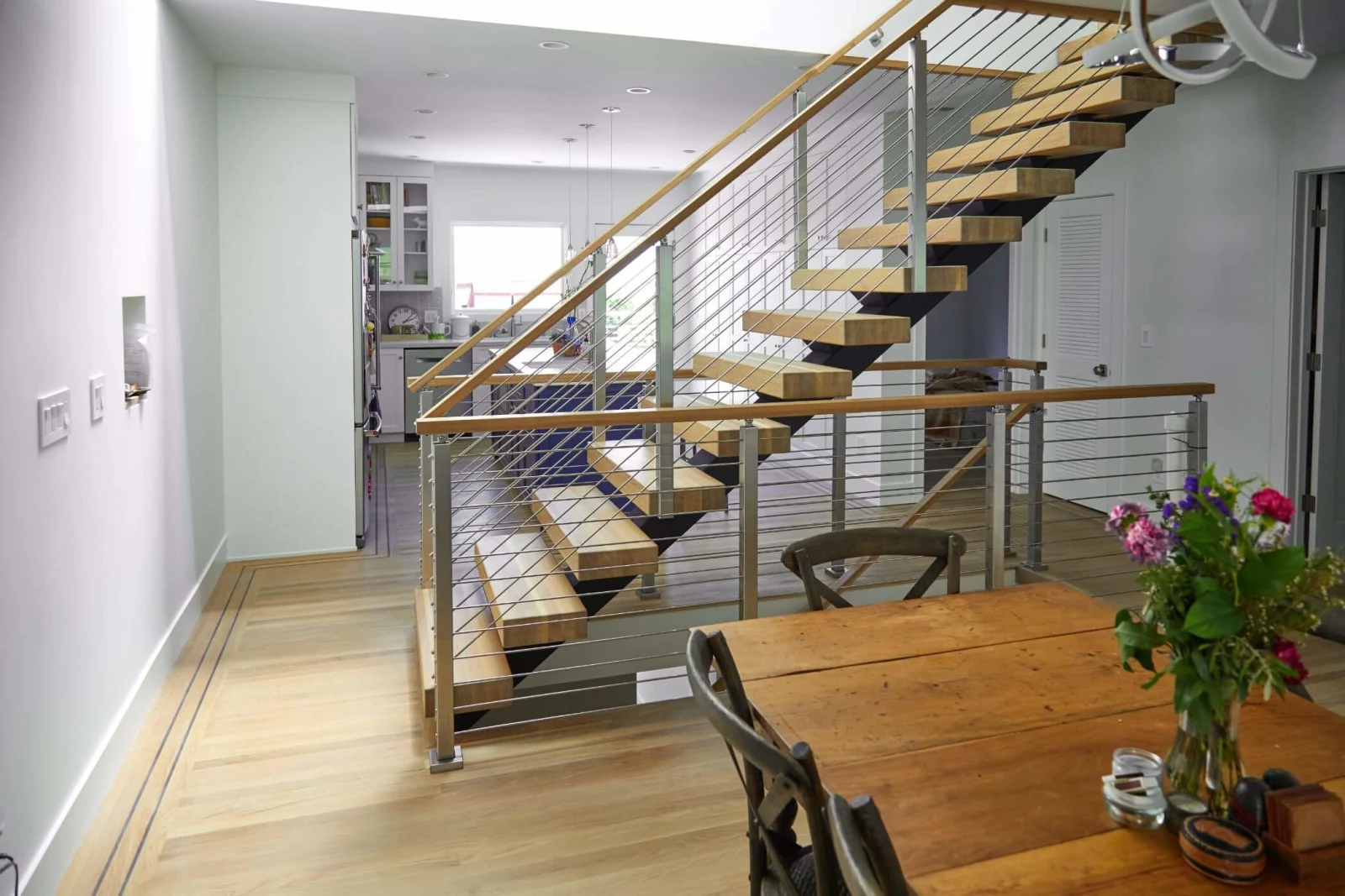 Open living space with thick stair treads and rod railing behind a dining table