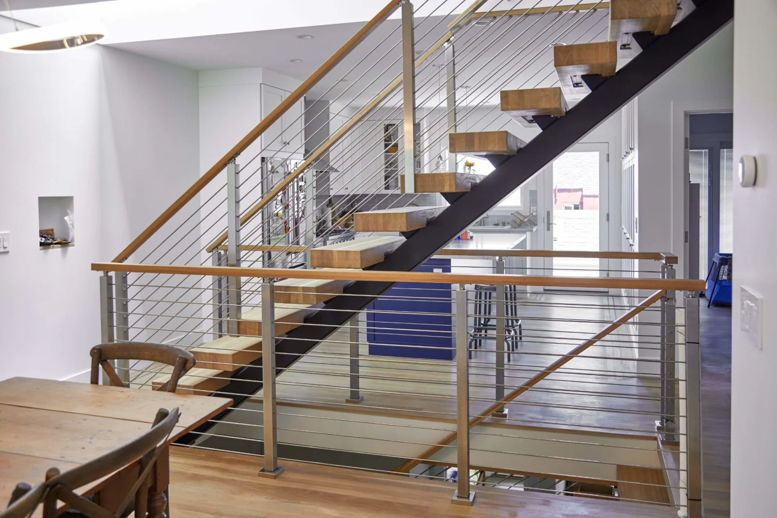 Wide view of a floating stair with rod railing and a dark steel stringer