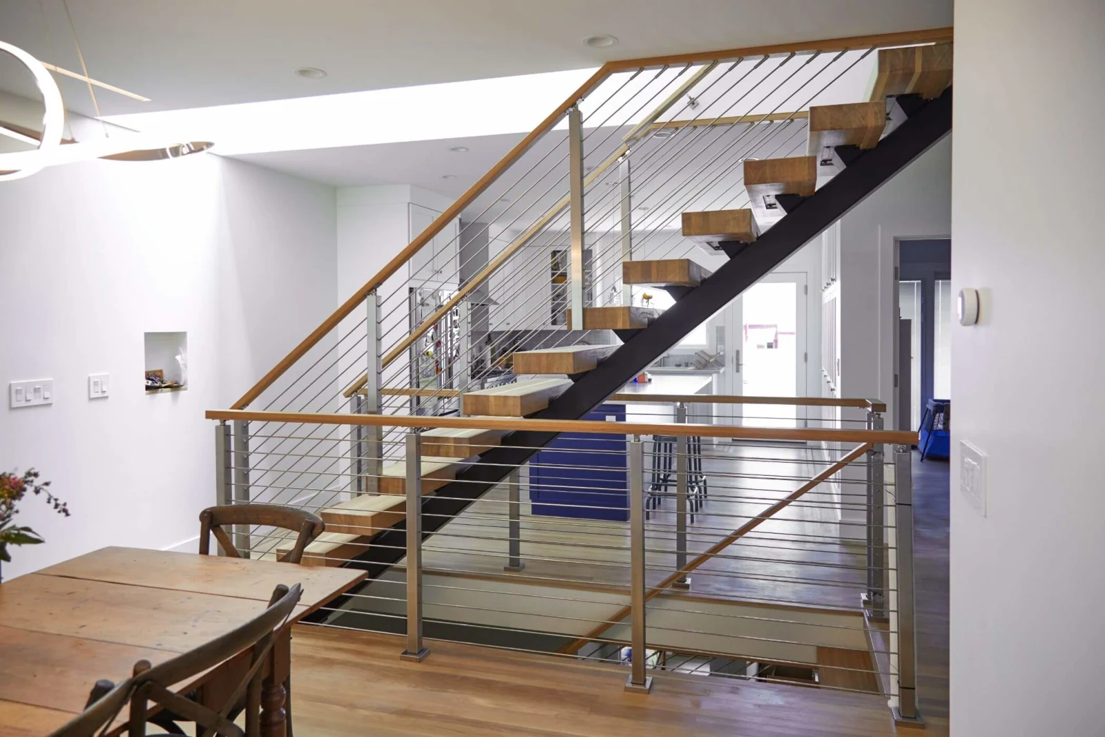 Rod-railed landing and stair treads lit by a sculptural ring ceiling fixture