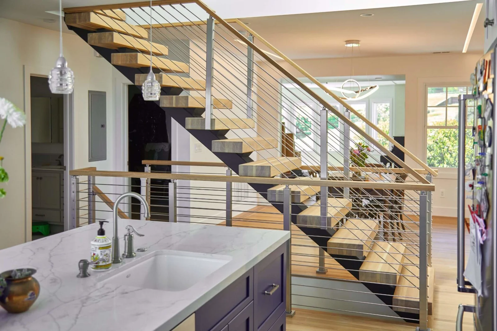 Floating stair with rod railing rising past a kitchen counter and pendant lights