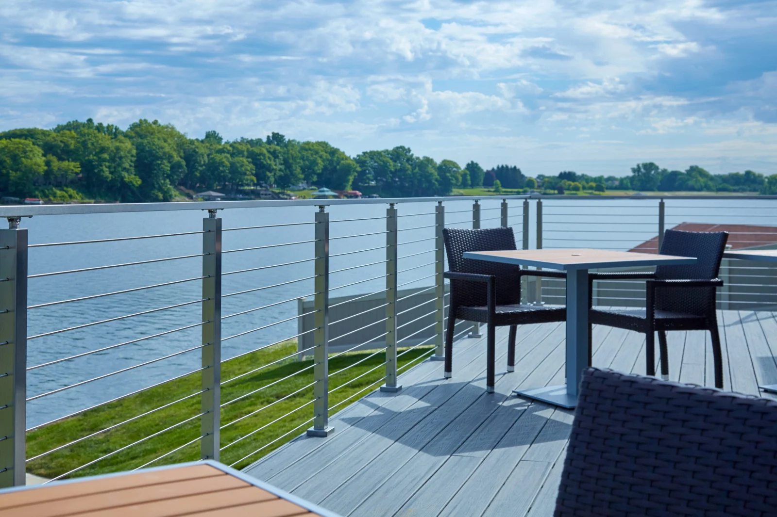 Lakeside deck with rod railing, patio table and chairs, water stretching to a treeline