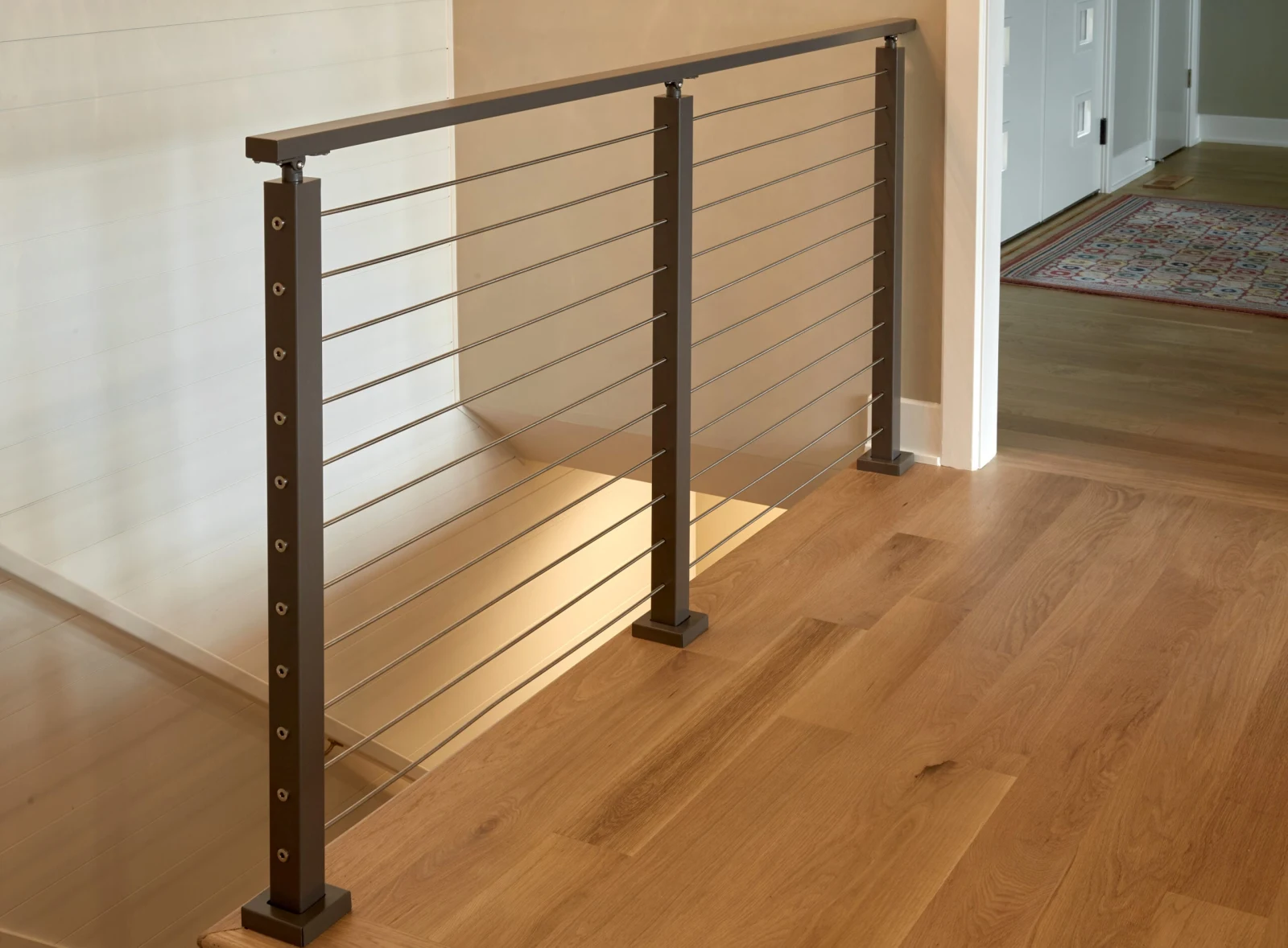 Bronze posts and stainless rods guarding a stair opening in a wood-floored hall