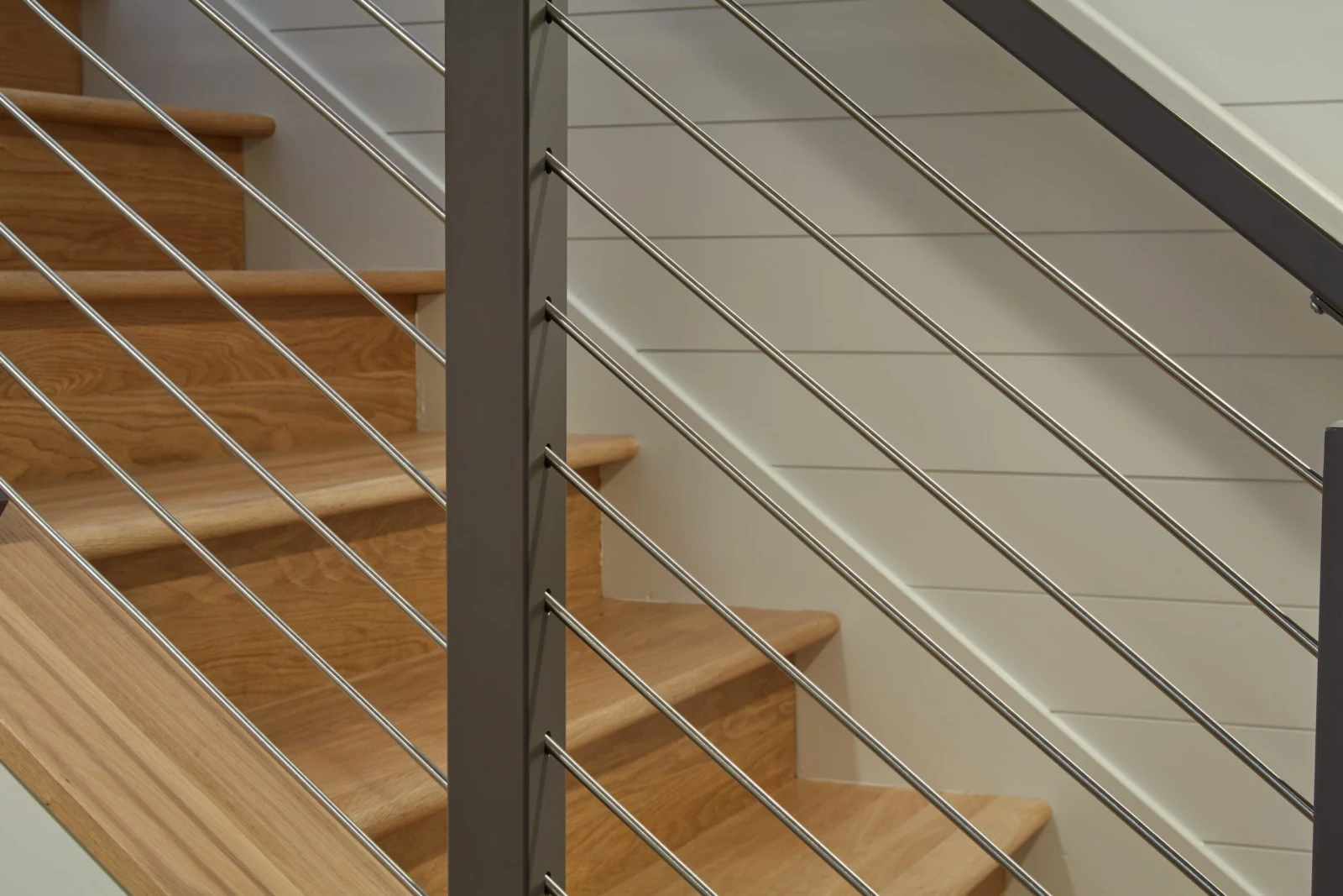 Tight detail of stainless rods crossing wood treads against a plain white wall