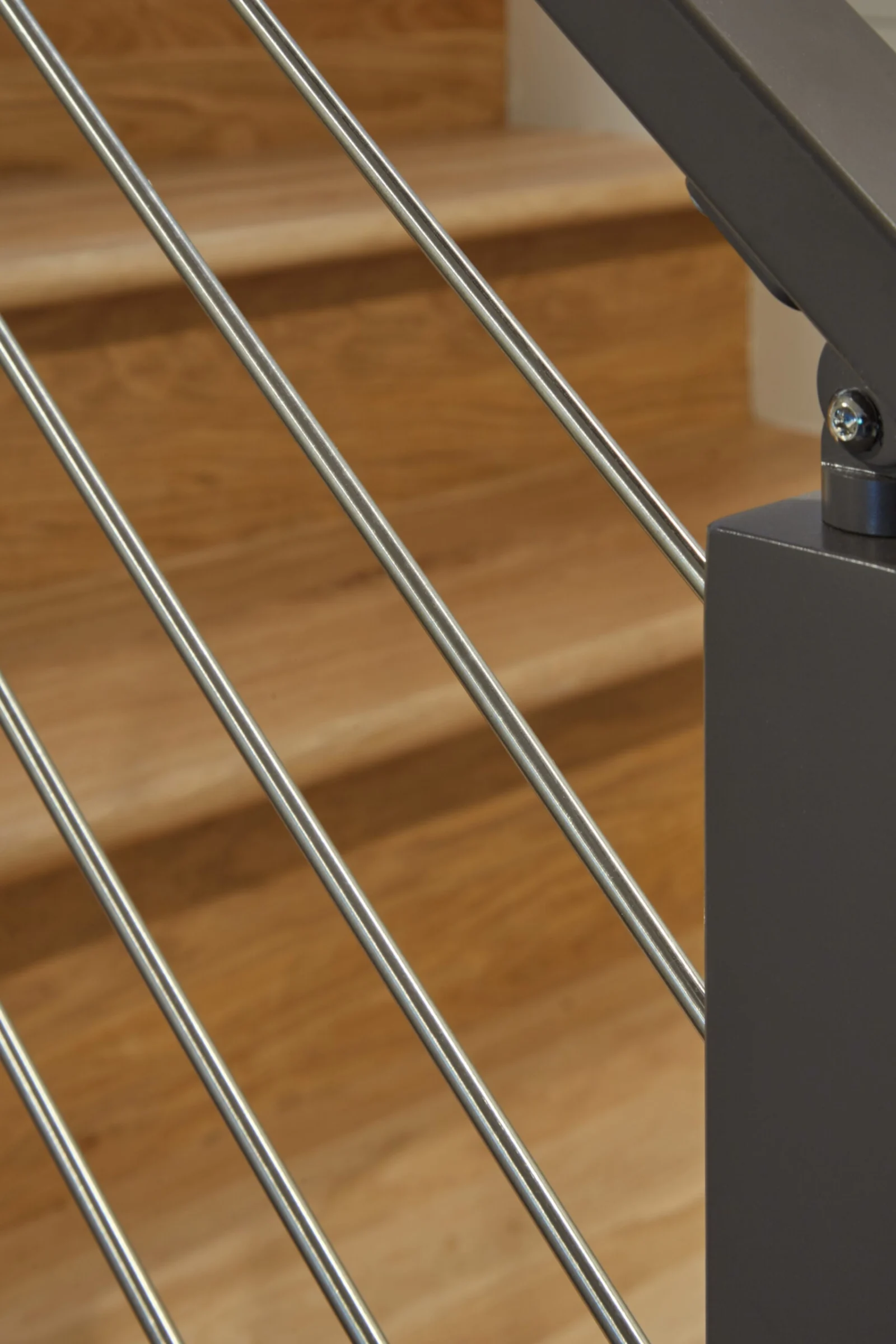Close view of angled rods meeting a dark handrail above light wood treads