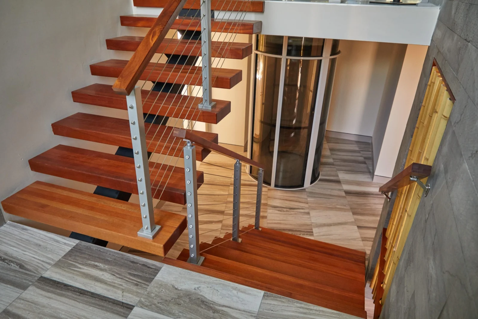 Looking down floating wood treads with rod railing toward a round glass elevator