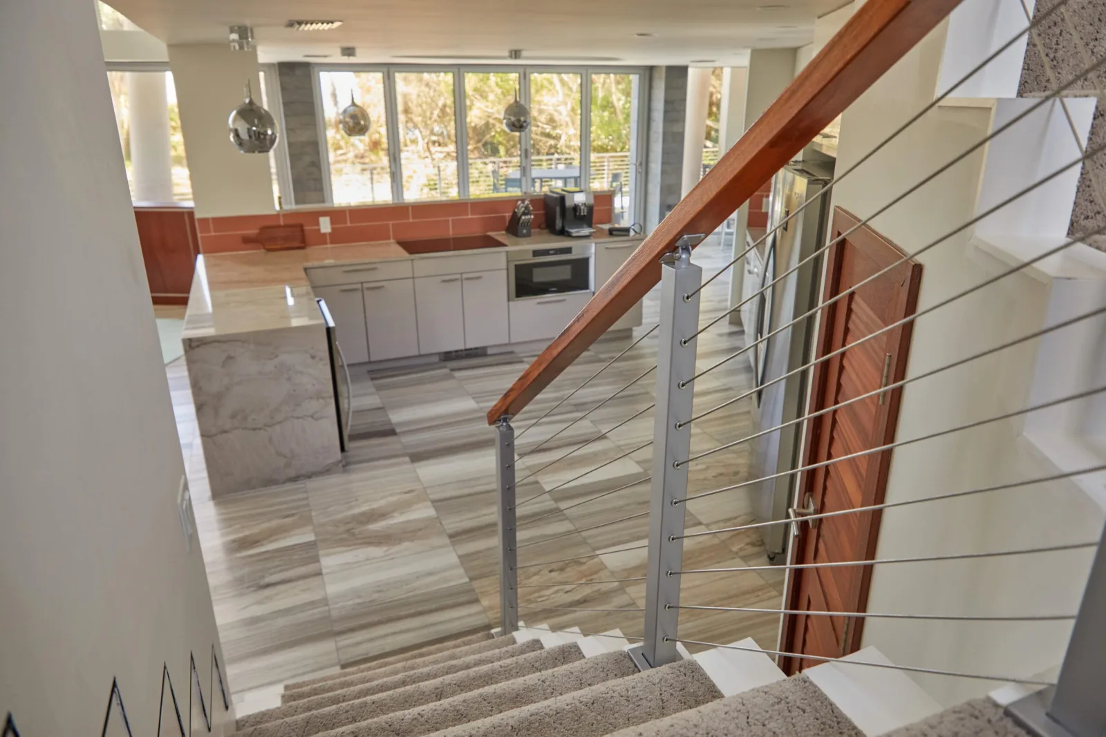 View down the stair over a wood top rail toward the open kitchen