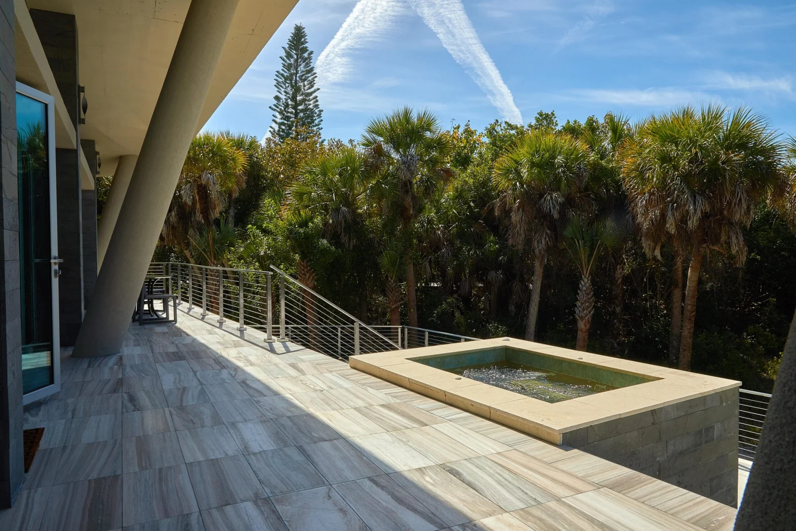 Rod railing wrapping a paved terrace beside a raised spa and palm trees