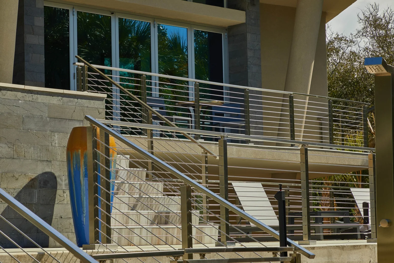 Raised deck railing with horizontal rods above a stone wall and leaning surfboards