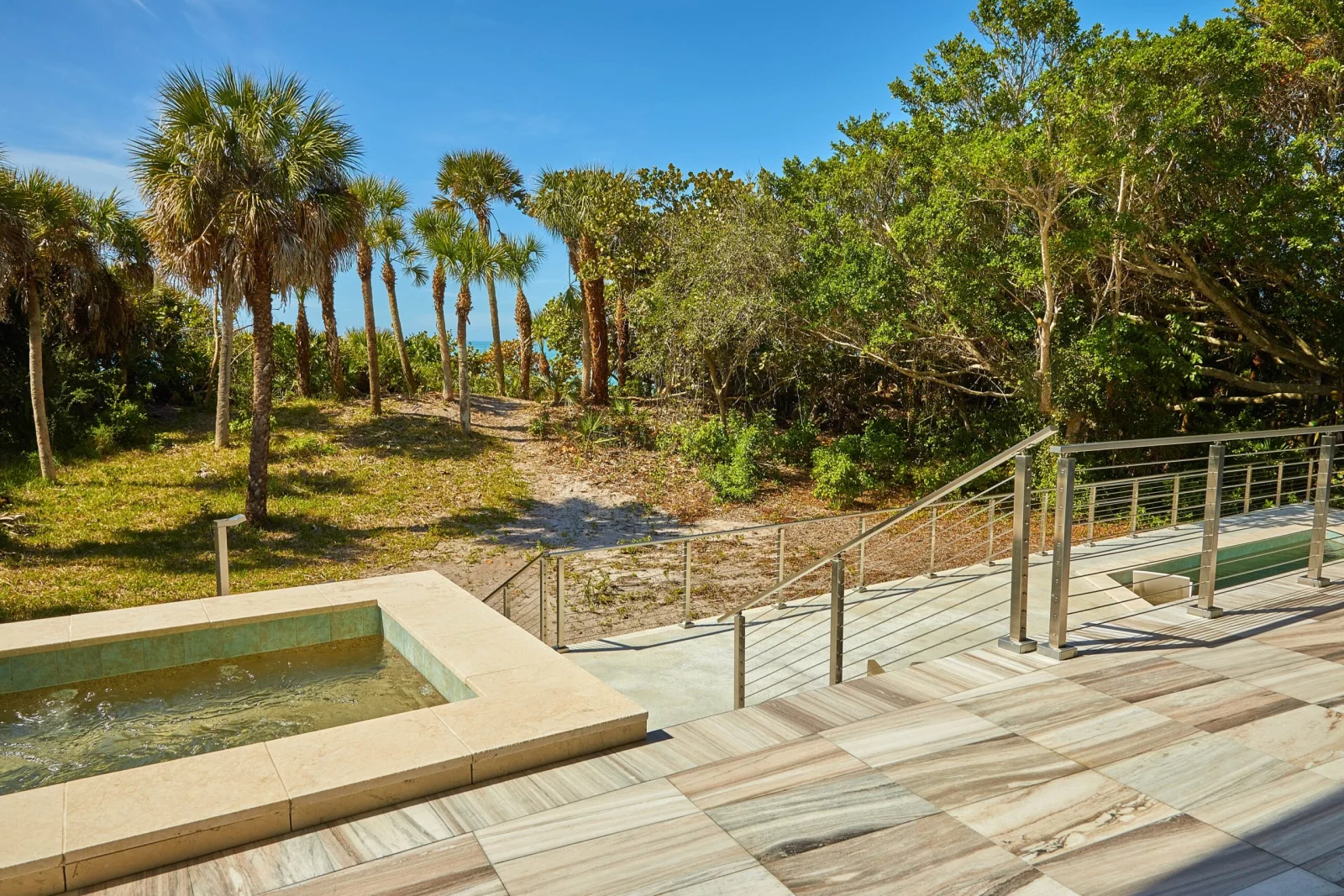 Stone pool deck with stainless rod railing edging a dune of palms
