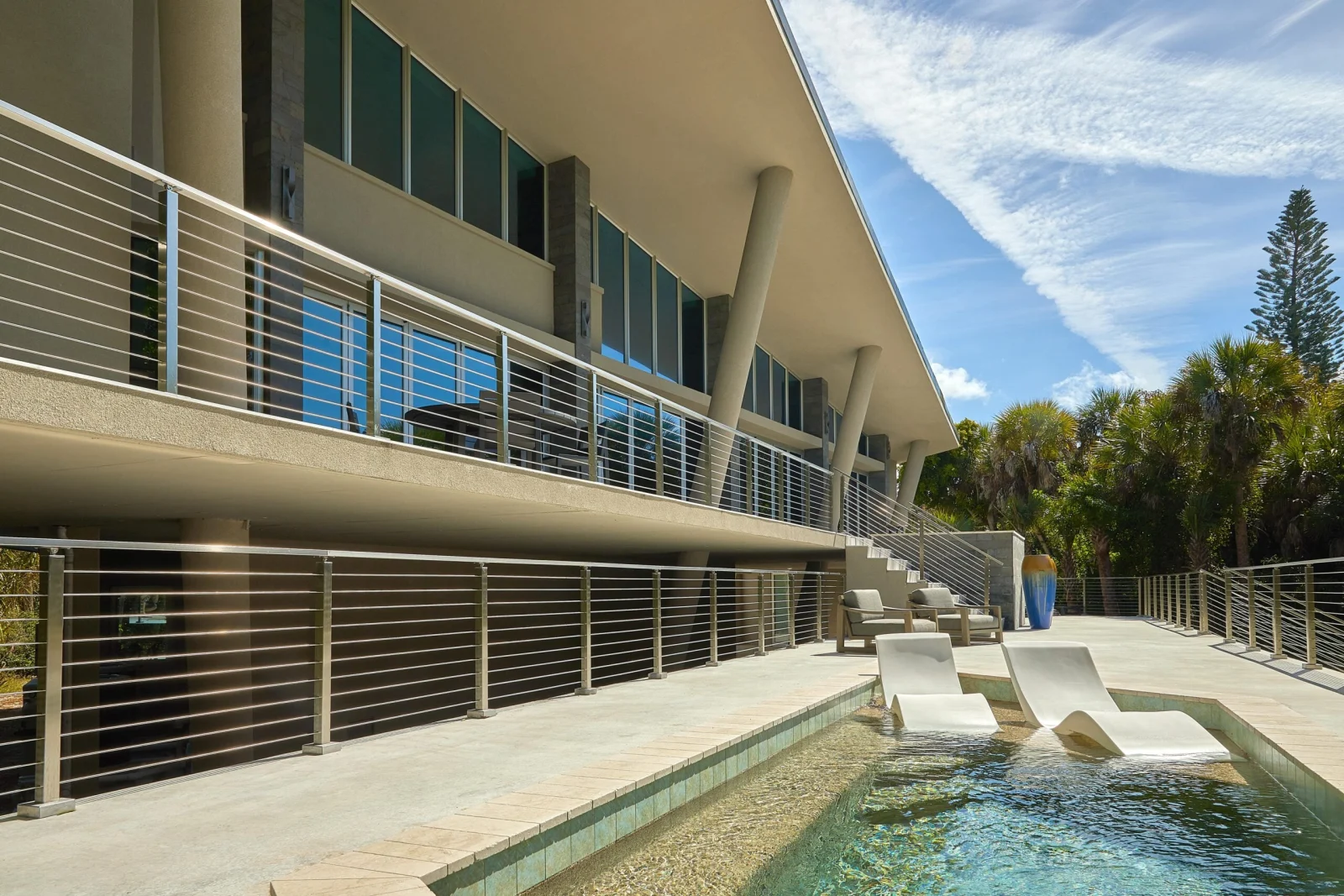 Angled run of rod railing on stacked balconies beside a pool with loungers
