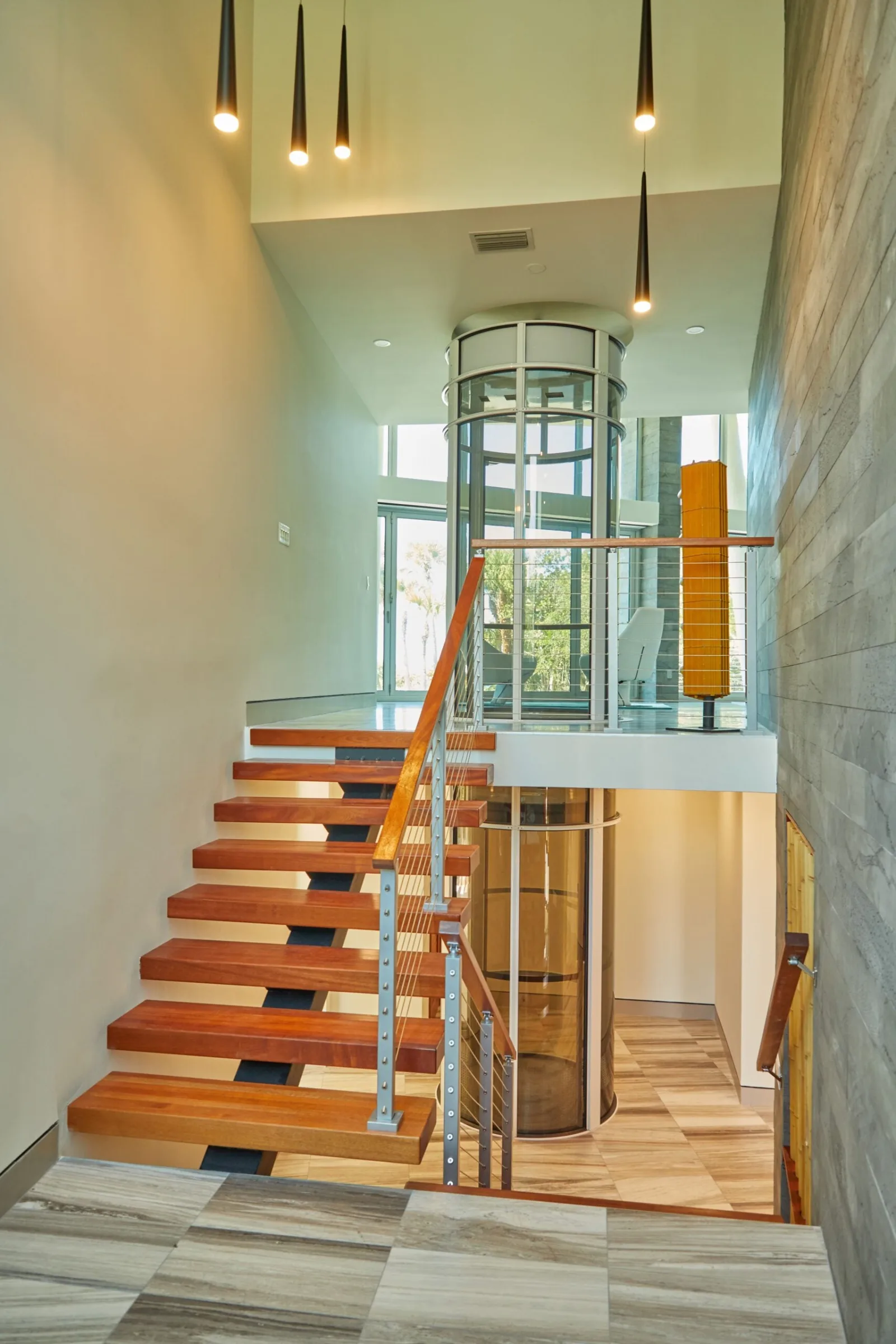 Interior stair with wood treads and stainless rod railing beside a glass elevator