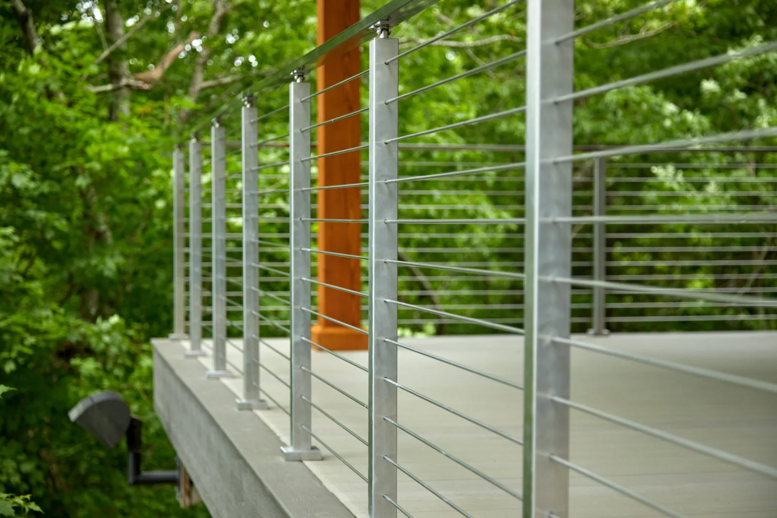 Row of stainless posts carrying horizontal rods along a forest-edge deck