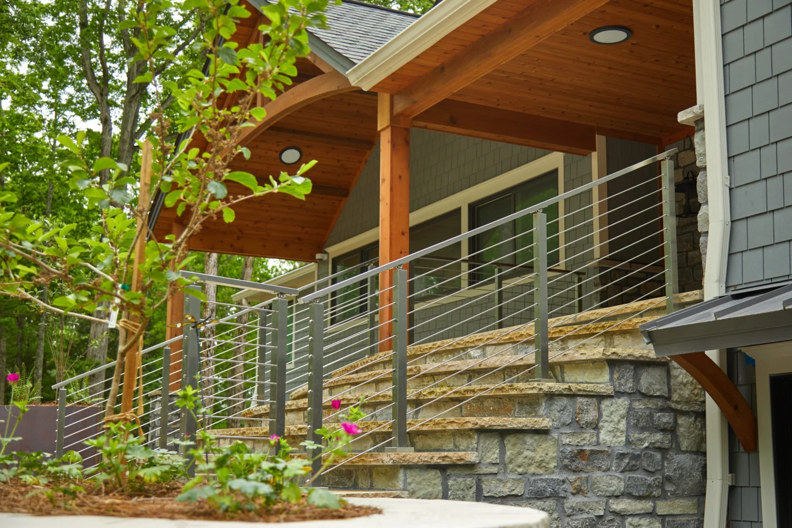 Stone steps rise to a timber-framed covered porch edged with stainless rod railing