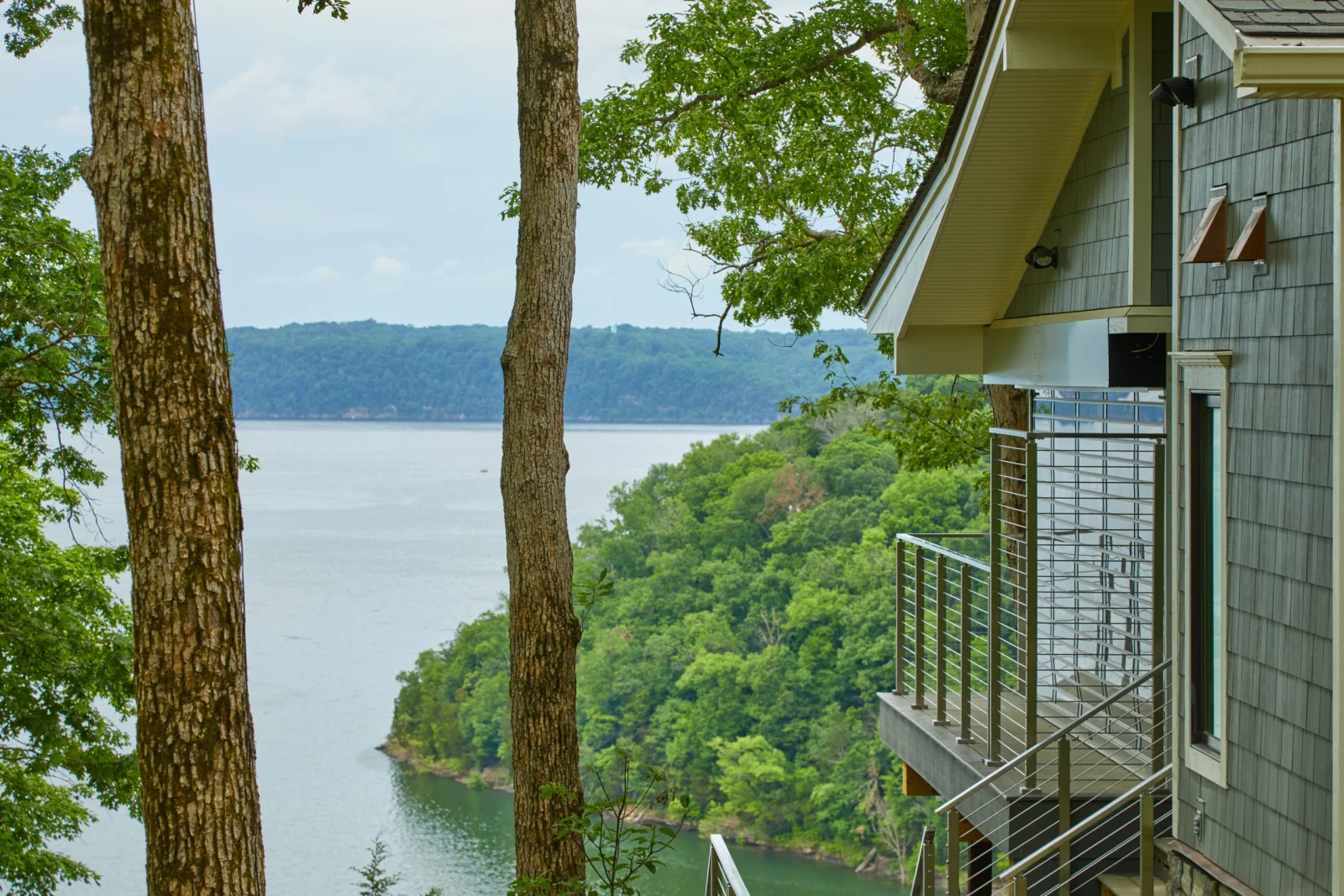 Hillside home with rod railing on its deck above a wooded lake inlet