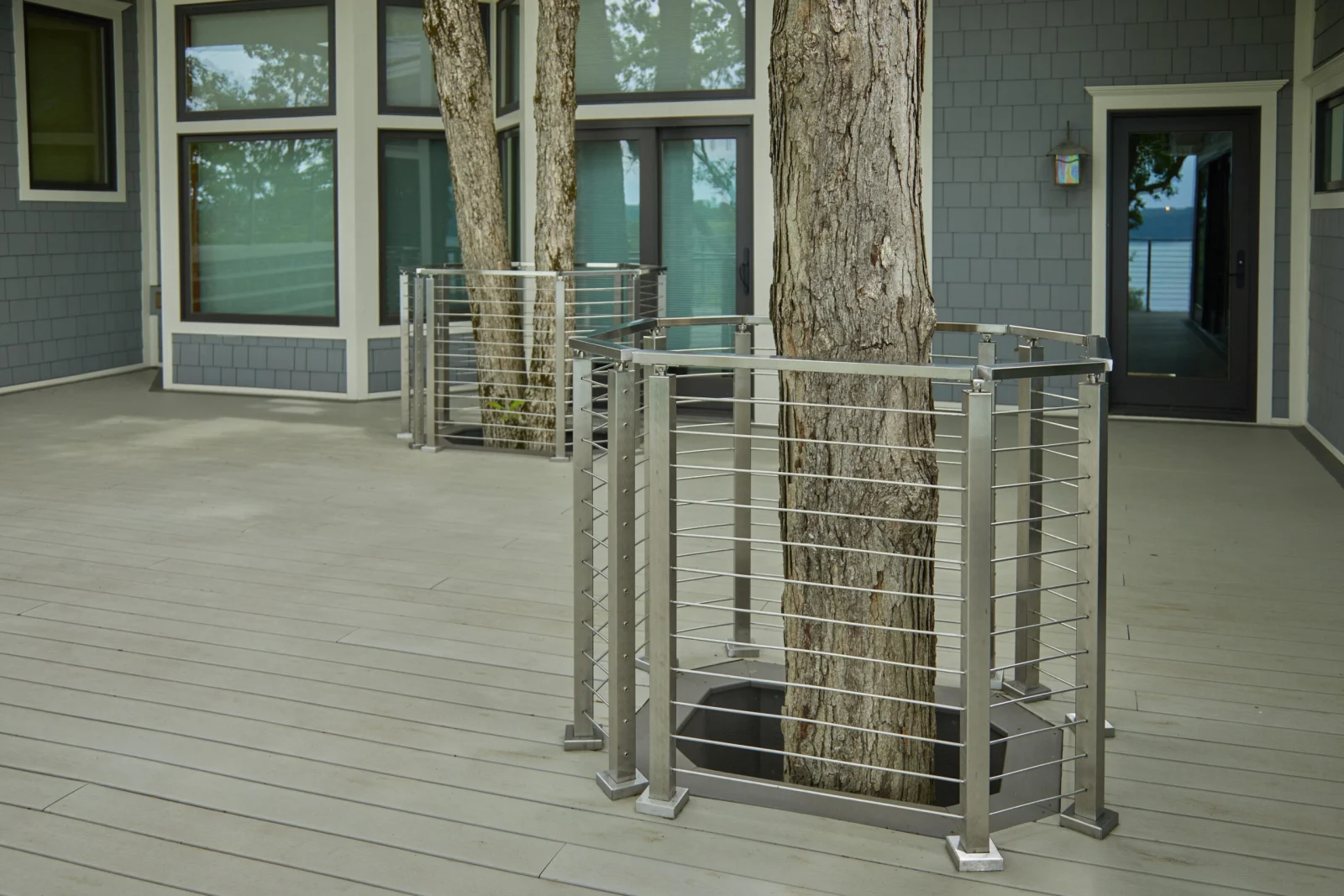 Rod railing enclosures wrapping mature trees that rise through a gray deck