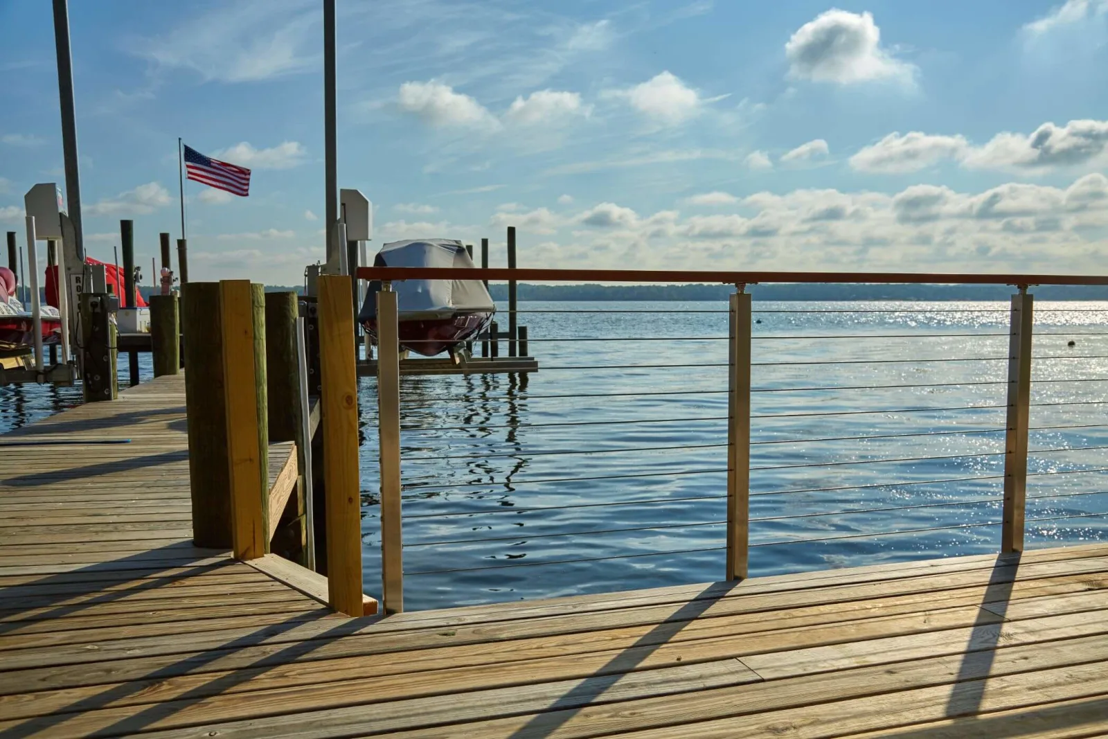 Dock railing of wood posts and thin rods beside a boat lift and open water