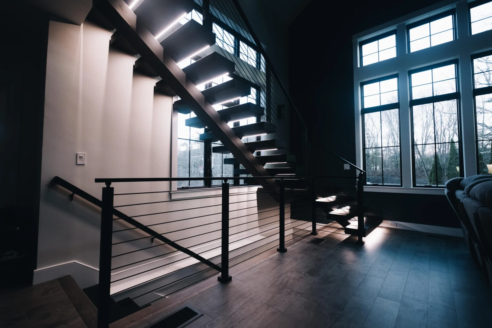 Dim interior at dusk with lit treads floating above a black rod railing