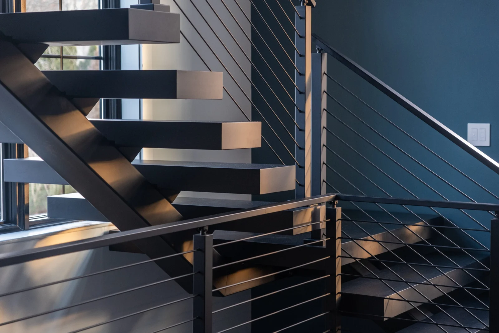 Treads and a turn landing enclosed by rod railing beside a deep blue wall