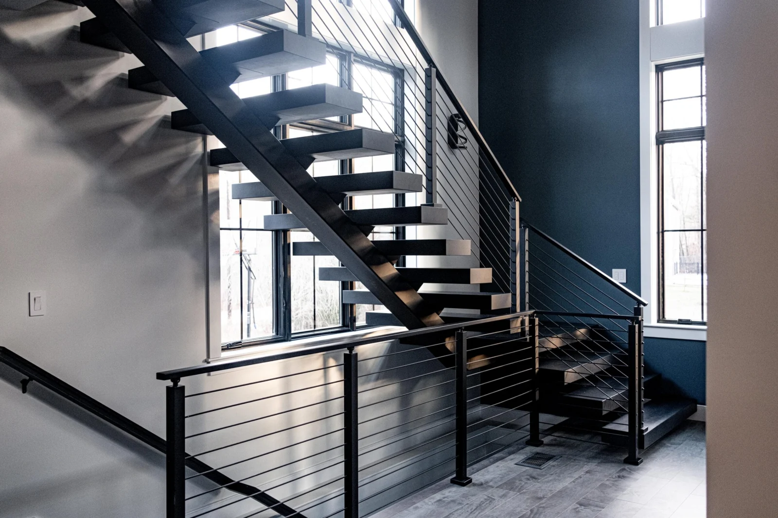 Daylight stairwell with pale treads, black rod railing and tall windows