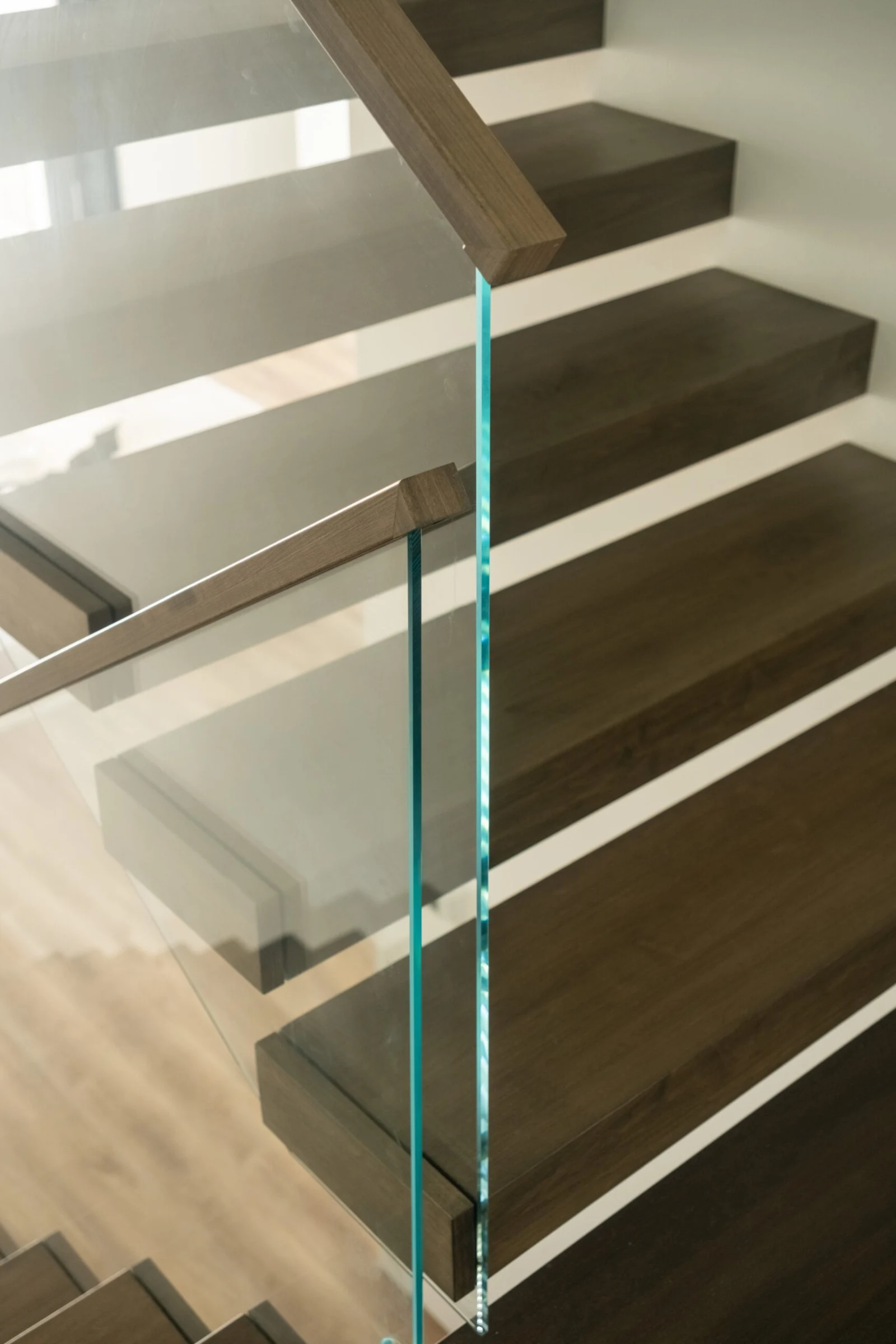Glass panel edge and wood handrail framing open risers above plank flooring