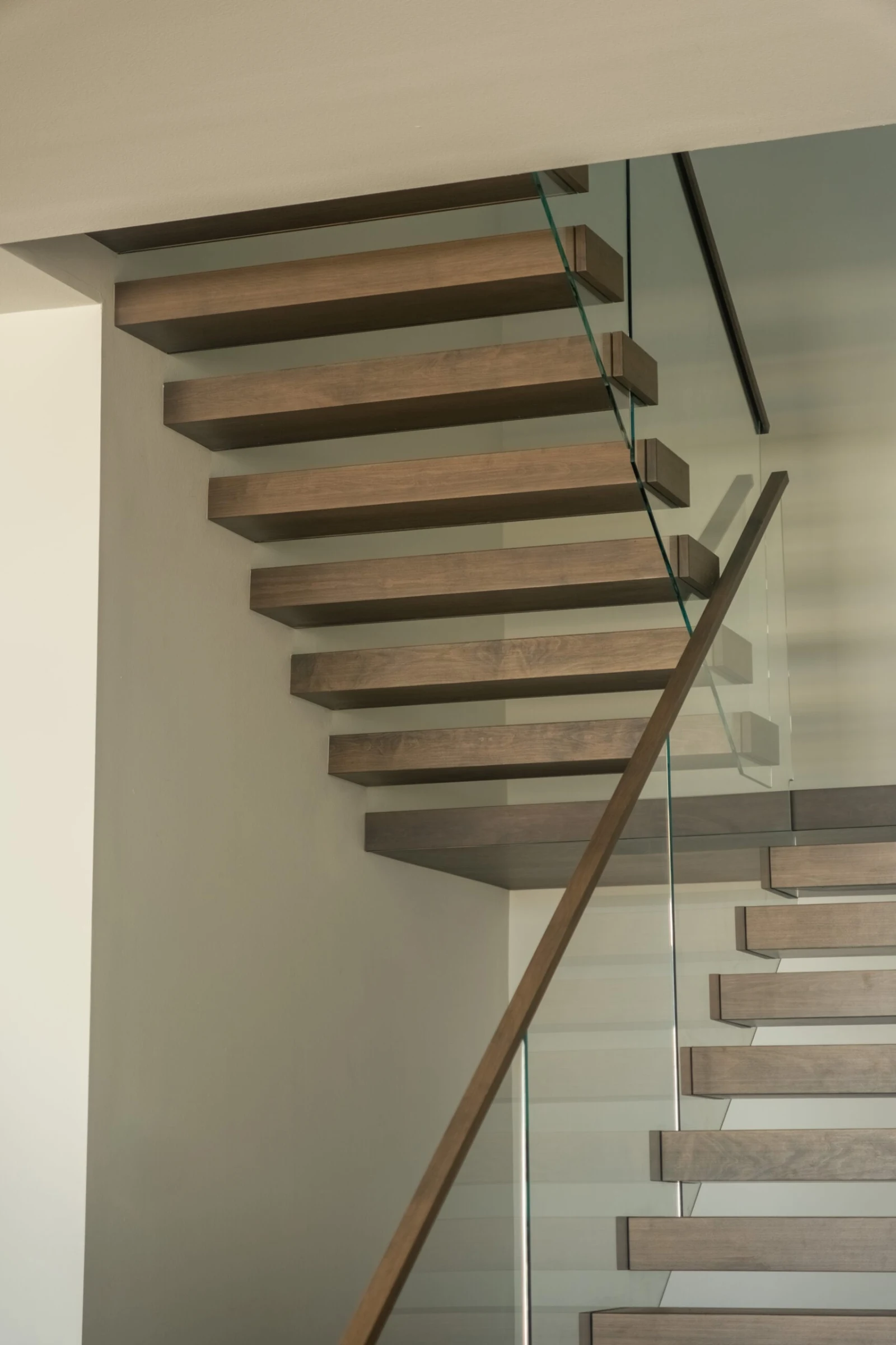 Looking up at cantilevered wood treads and glass railing from below the landing