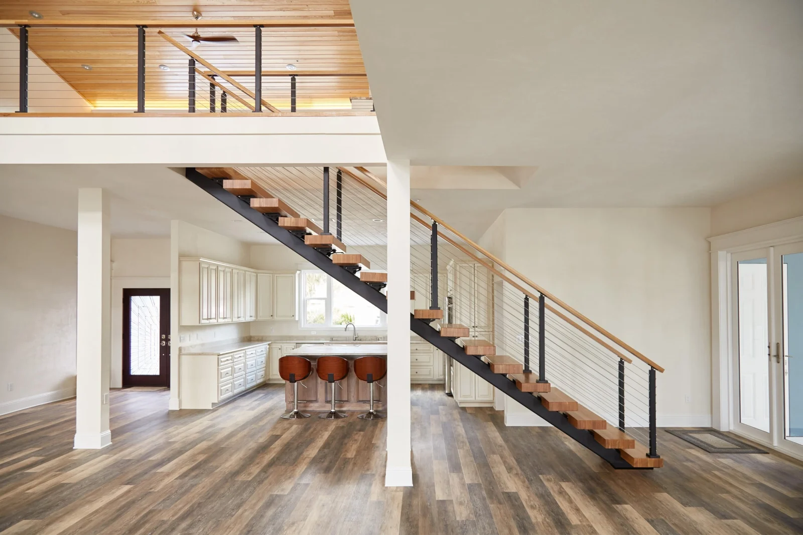 Open floor plan with a cable railing stair rising past a wood-lined loft balcony