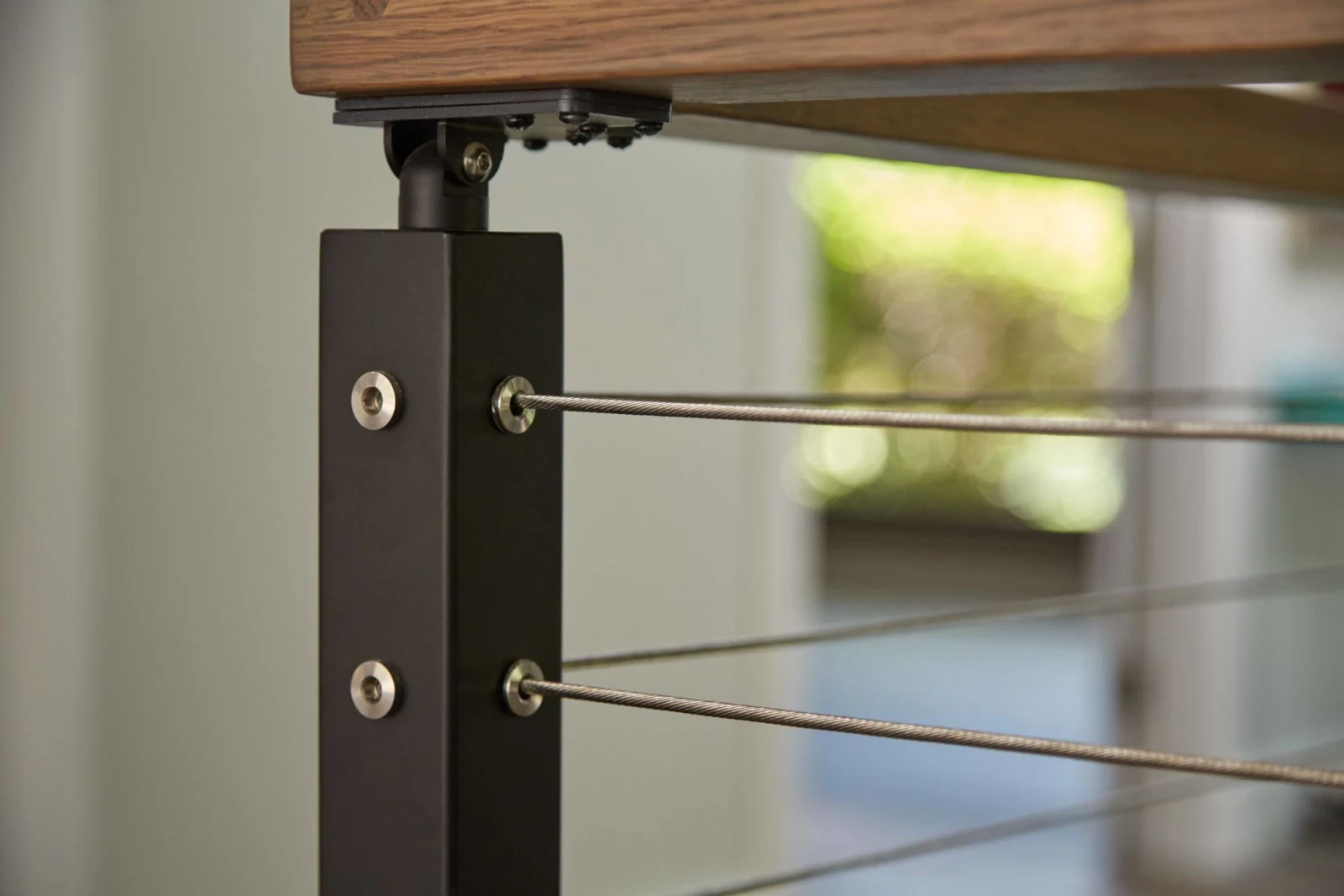 Black post detail with swaged cable ends beneath a wood top rail