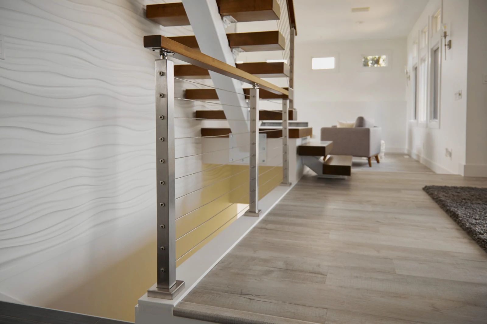 Stainless steel cable railing and wood-capped handrail running beside the white stair stringer