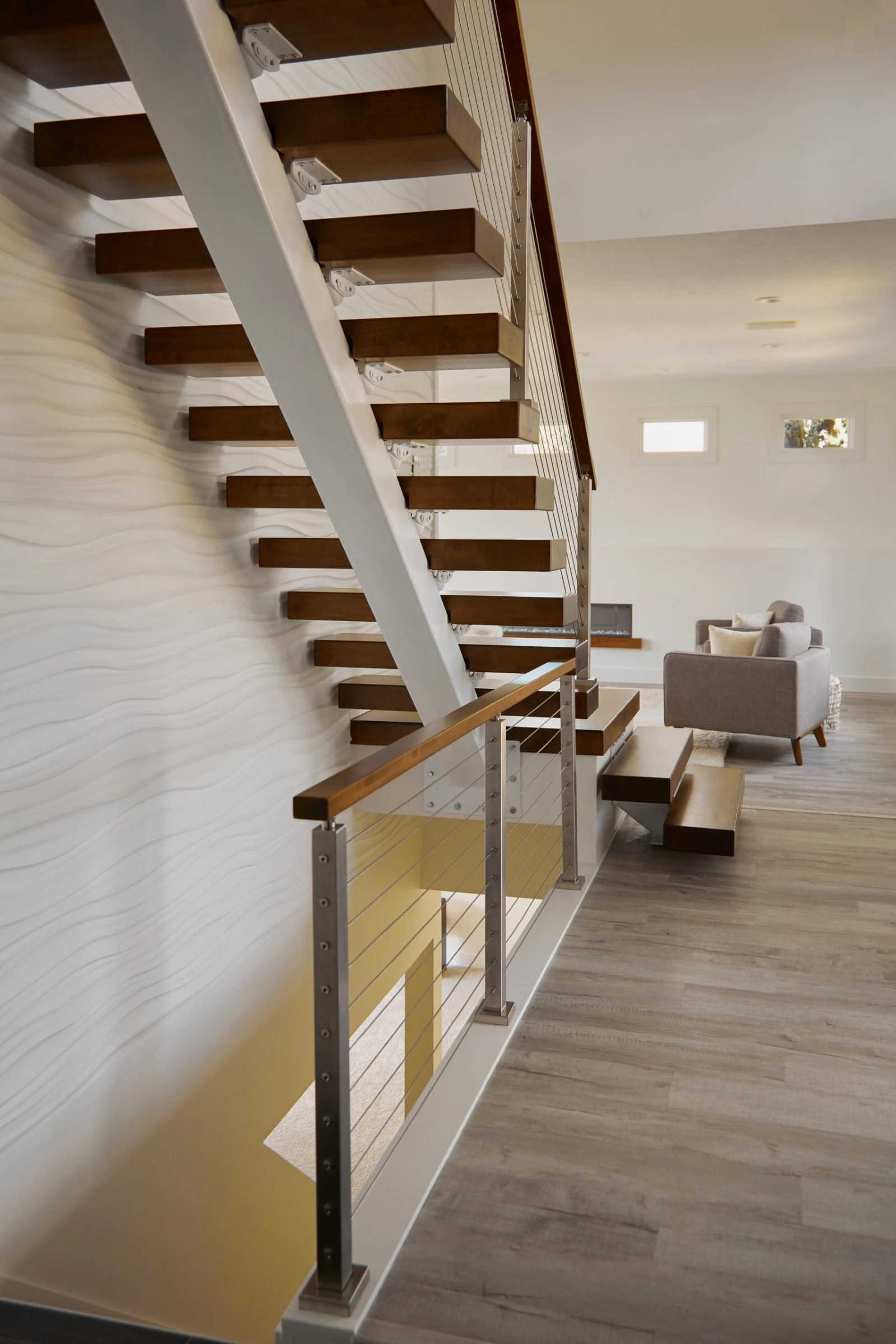 Full flight of open-riser wood treads climbing a textured white wall to the upper floor