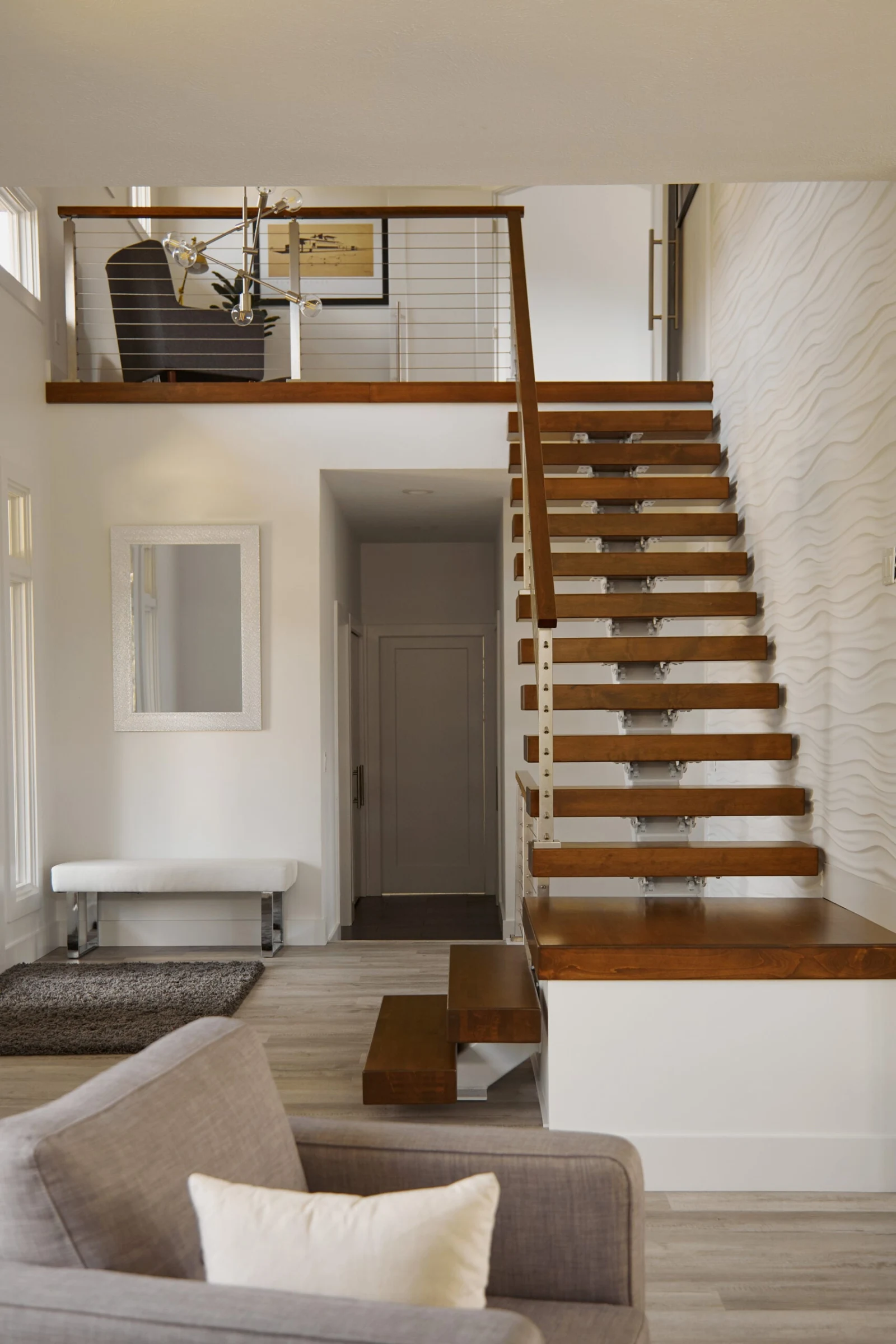 Floating stair and cable-railed upper balcony seen across a two-story open living space