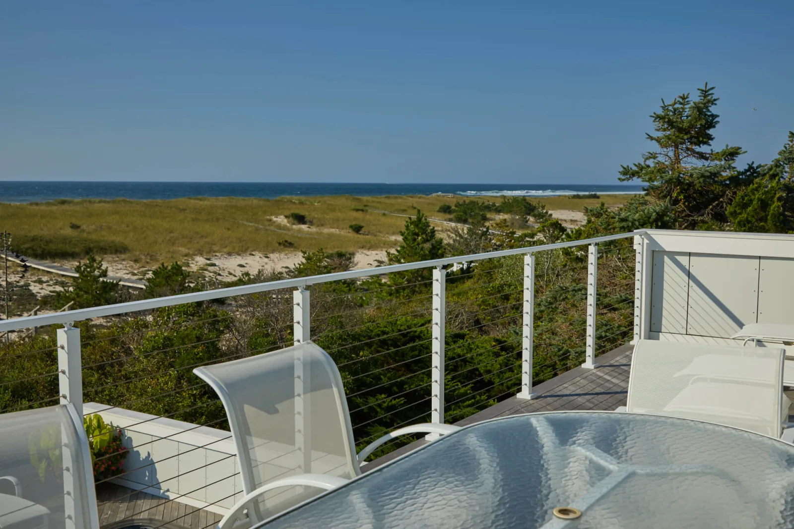 Dining table on the deck with cable railing framing an ocean view