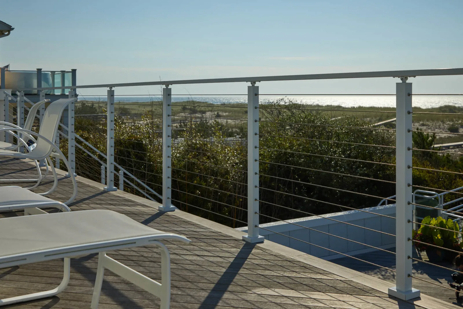 Cable railing along a rooftop deck lined with white lounge chairs